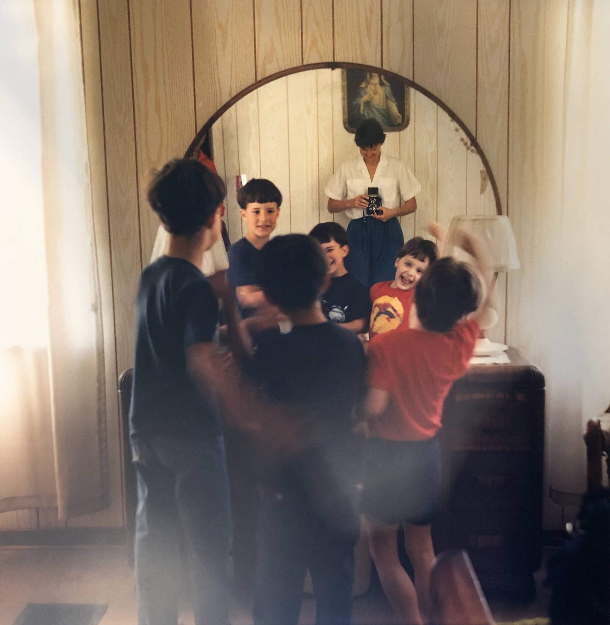Photograph shows the photographer taking the image in the mirror with three young boys posing for the picture through the mirror.